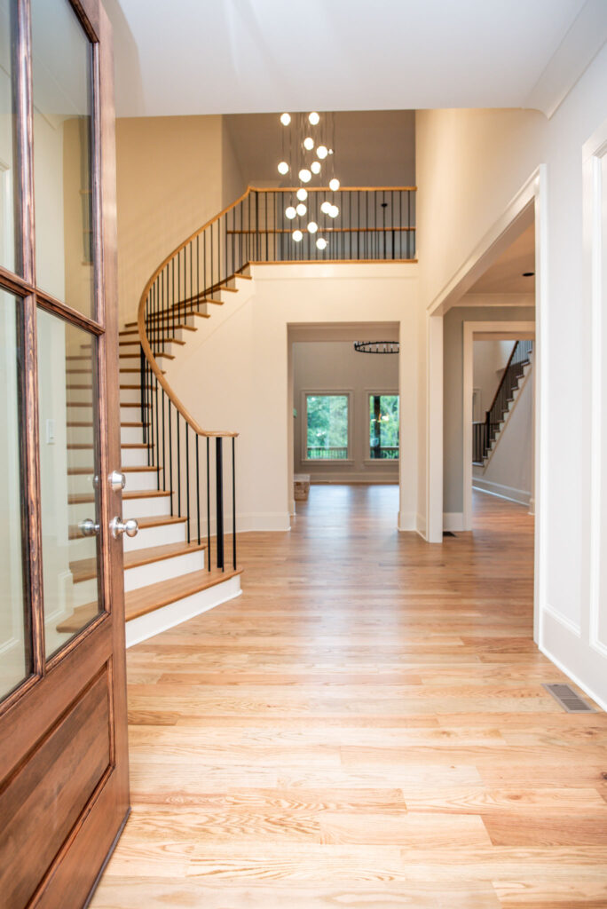 Bright entry foyer with curved staircase, hardwood floors, glass front door, and modern hanging chandelier