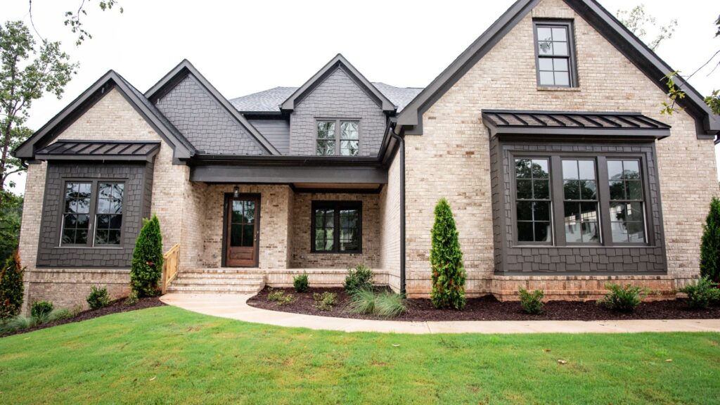 Modern brick home exterior with dark gray gables, large windows, landscaped front yard, and curved concrete walkway to the front porch