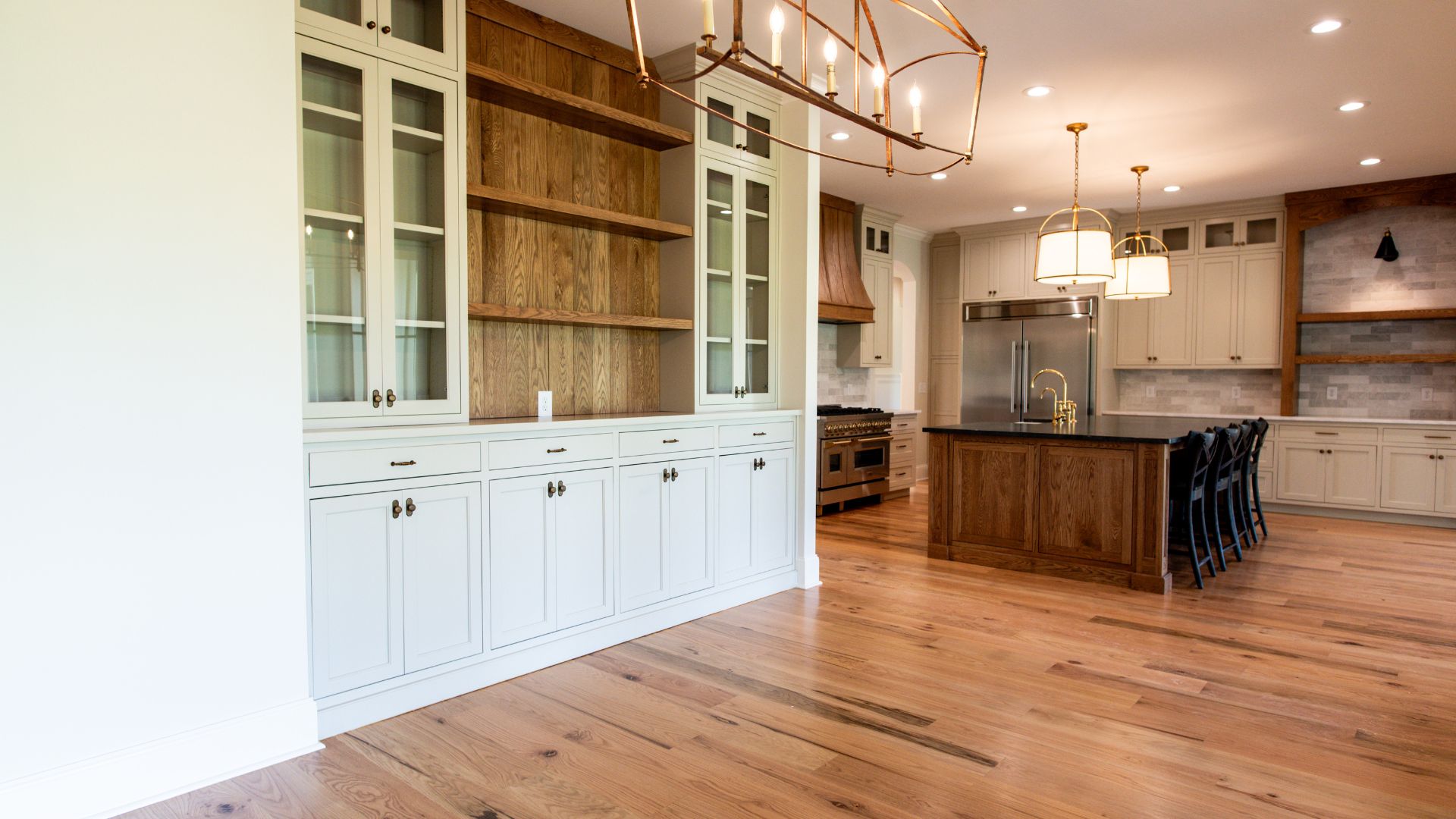 Custom kitchen with built-in cabinets and open wood shelving, large island with bar stools, pendant lighting, and wide plank hardwood floors