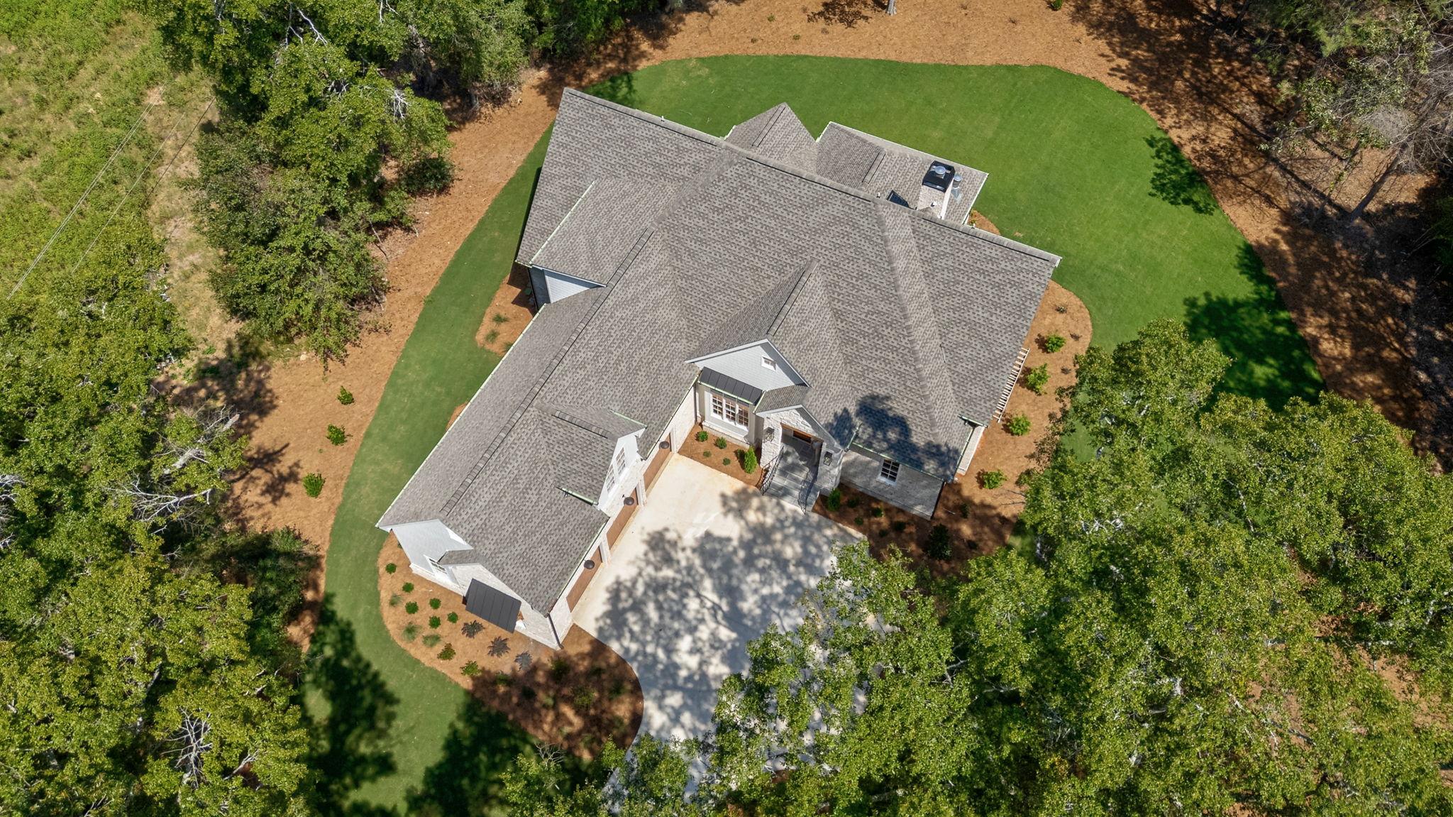 Aerial view of a custom home with a large shingle roof, curved driveway, and landscaped yard surrounded by mature trees